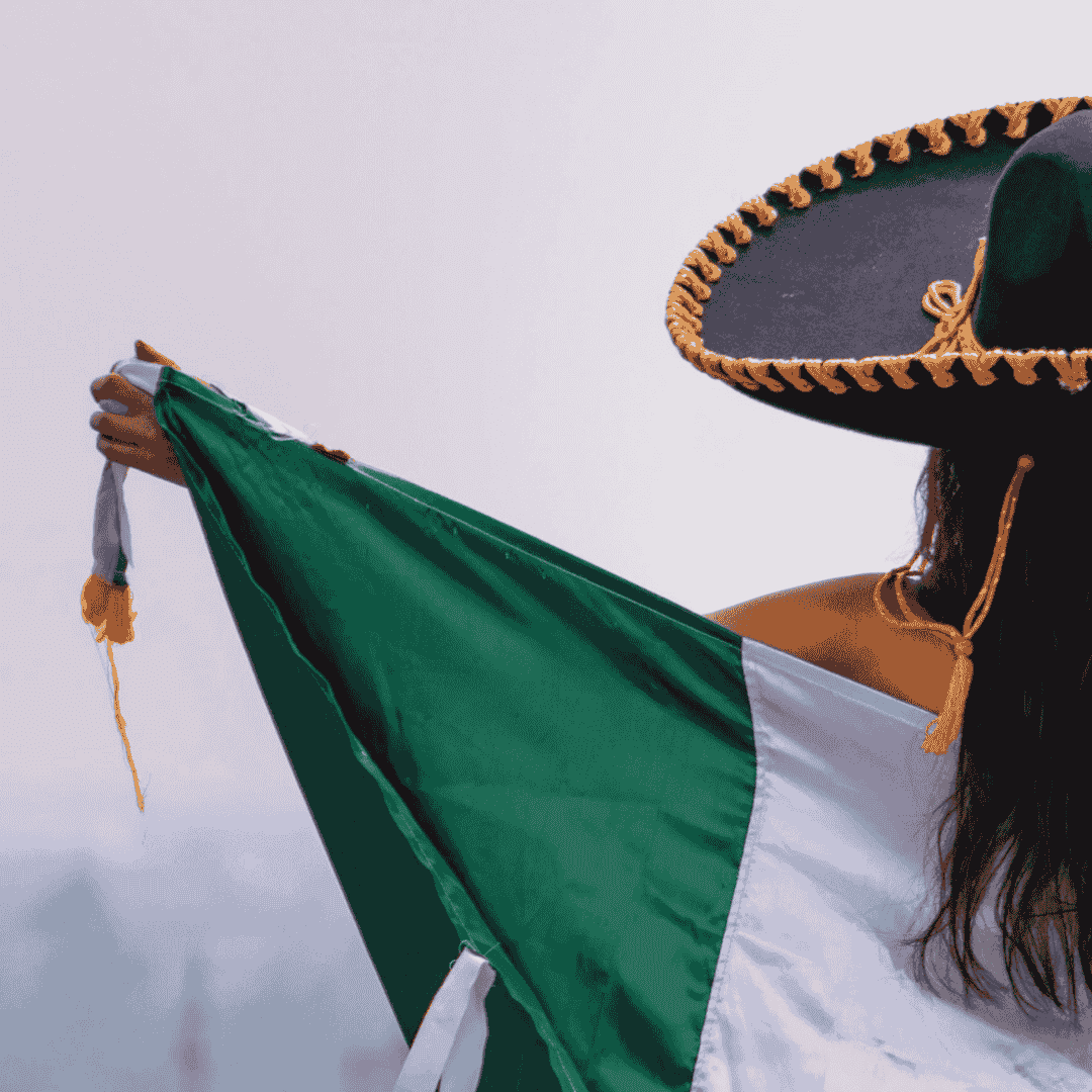 mujer de espaldas ondeando la bandera de Mexico y usando un sombrero de mariachi
