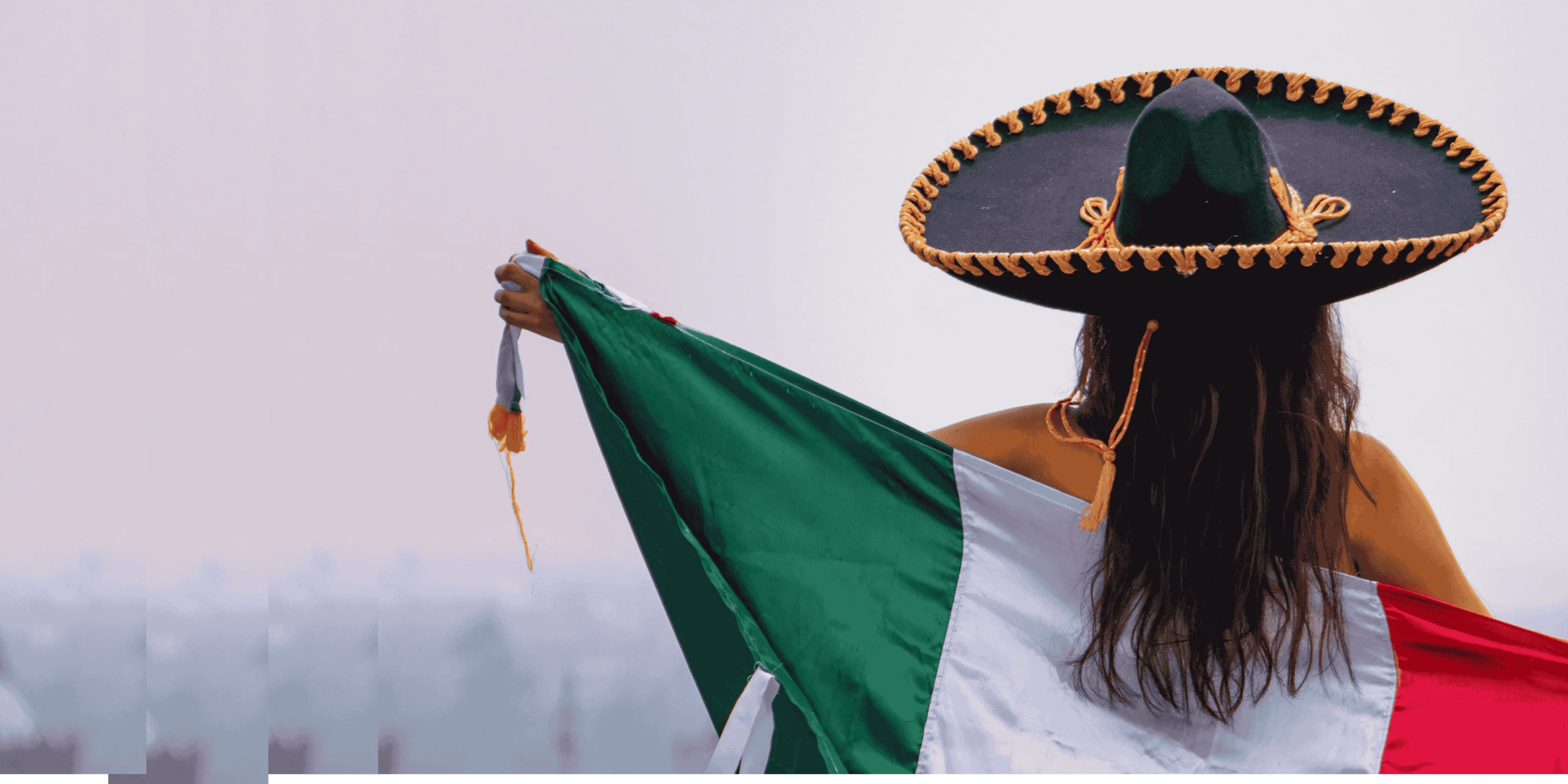 mujer usando un sombrero de mariachi, de espaldas ondeando la bandera de Mexico