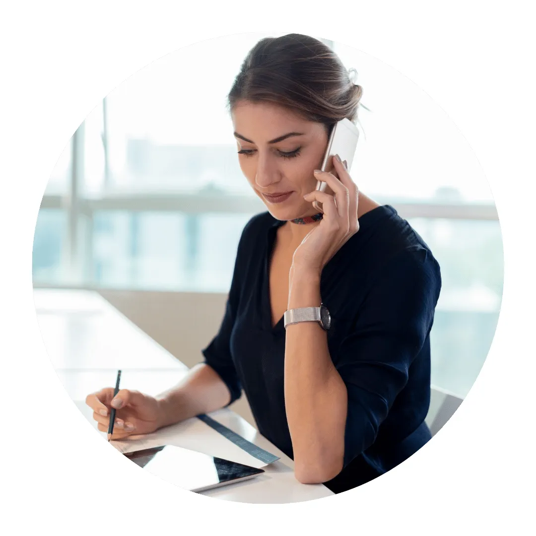 Businesswoman calling a customer on her phone while taking notes